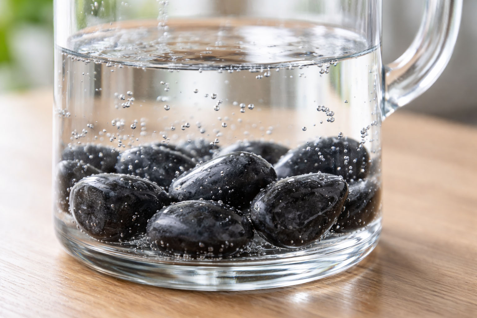Piedras de Shungit de élite en el fondo de una jarra de cristal con agua pura y burbujas, mostrando el proceso de filtrado natural y vitalización.